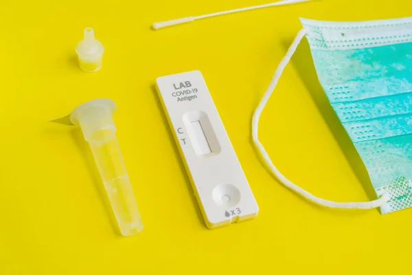 A set of COVID-19 rapid self test kits with medical equipment isolated on yellow background. Antigen or Antibody test. Face mask, Thermometer and pulse oximeter. Virus disease healthcare check.