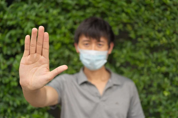 Portrait of ill young Asian man. Sick person wearing a face mask, using a hand to stop in medical treatment and healthcare isolated. Coronavirus. People lifestyle activity. Social distancing. Outdoor