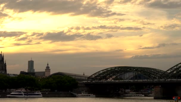 ライトアップされたケルン大聖堂の真後ろに沈む4Kビデオクリップとドイツのライン川にかかるホーエンツォレルン橋の列車 — ストック動画