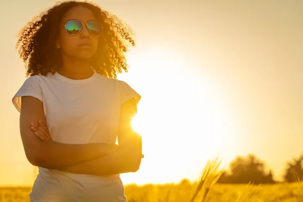 年轻的非洲裔美国少女 身穿白色T恤衫 太阳镜和日落时被太阳照得发亮的背 双手交叉抱在田野里 美丽的混血种族 — 图库照片