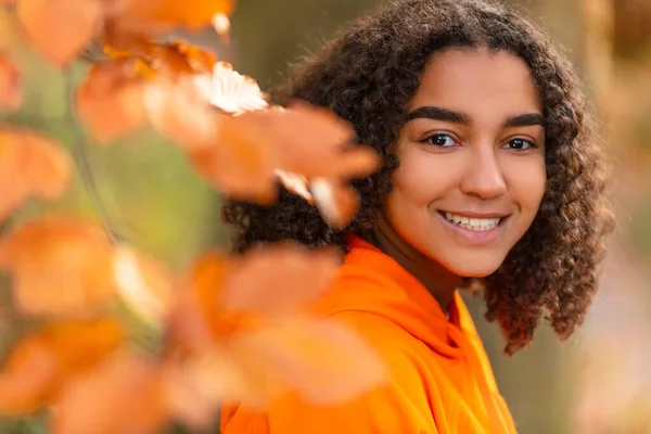 美しい幸せな混合レースの屋外ポートレート誕生アフリカ系アメリカ人の女の子ティーン女性若いです女性笑顔で完璧な歯を身に着けていますオレンジ色のパーカー秋または秋の黄金の葉に囲まれて — ストック写真