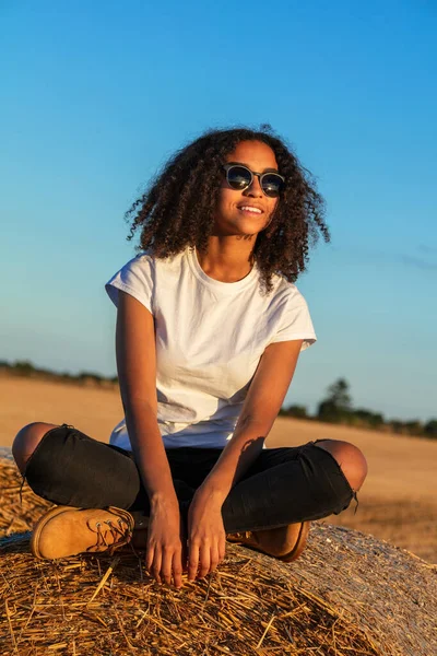 美丽的非洲裔美国少女 穿着白色T恤 戴着太阳镜 坐在田里的干草捆上 夕阳西下 — 图库照片