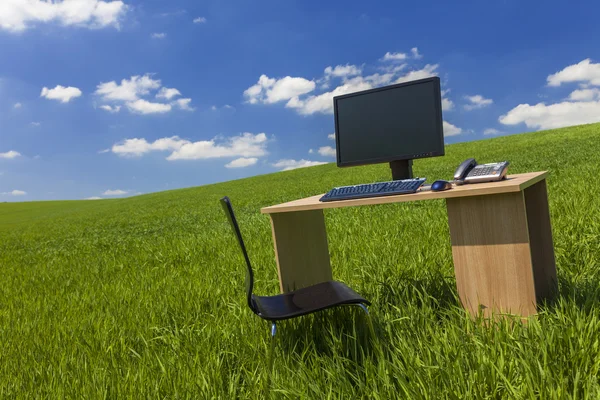 Scrivania e computer in campo verde con cielo blu — Foto Stock
