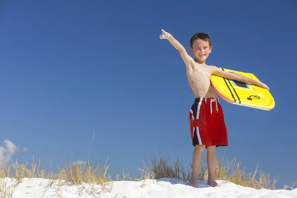 Junge männliches Kind zeigt mit Surfbrett auf Strand — Stockfoto