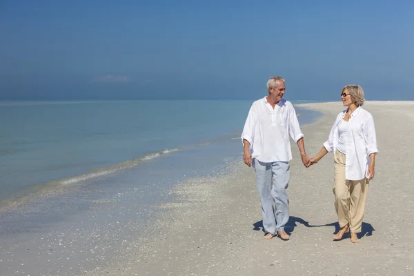 Счастливая пожилая пара гуляет, держа за руки пляж — стоковое фото