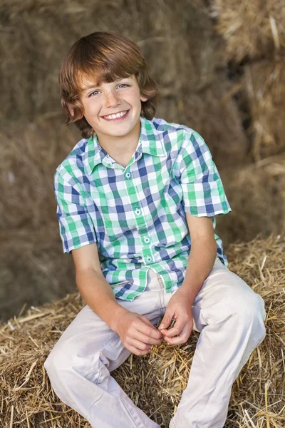 Jovem menino feliz sentado sorrindo em fardos de feno — Fotografia de Stock
