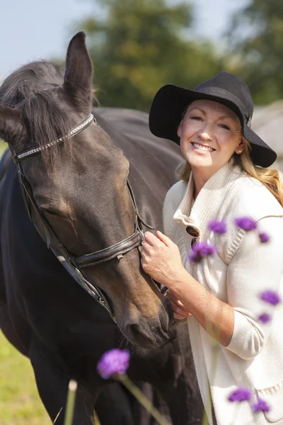 Mulher de chapéu preto atordoando seu cavalo — Fotografia de Stock