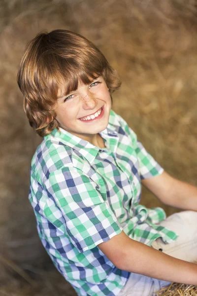 Menino feliz criança sentada sorrindo em fardos de feno — Fotografia de Stock