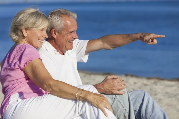 Pareja mayor sentada en la playa señalando — Foto de Stock