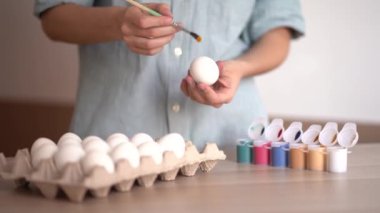 Dişi eller, beyaz arka planda koyu sarı boya ile yumurtayı boyuyor. Paskalya için hazırlanıyorum. Yumurta boyuyorum, mutlu Paskalyalar.