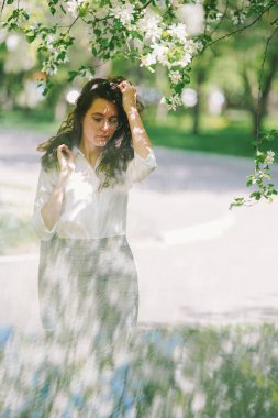 Kız saçlarını çiçek açan elma ağacının altında düzeltiyor.