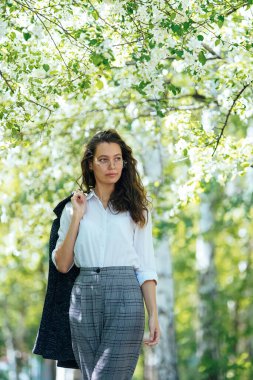 Omzunda ceketi olan kız çiçek açan elma ağaçlarının altında.
