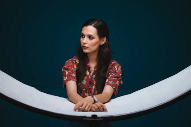 Makyajlı kız stüdyoda yansıtıcıya yaslanıyor.