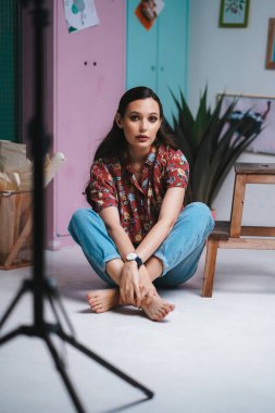 Makyajlı ve stil sahibi bir kız yerde bacak bacak bacak üstüne atmış oturuyor.