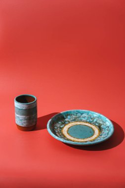 Turkuaz seramik bardak ve parlak kırmızı arka planda plaka.