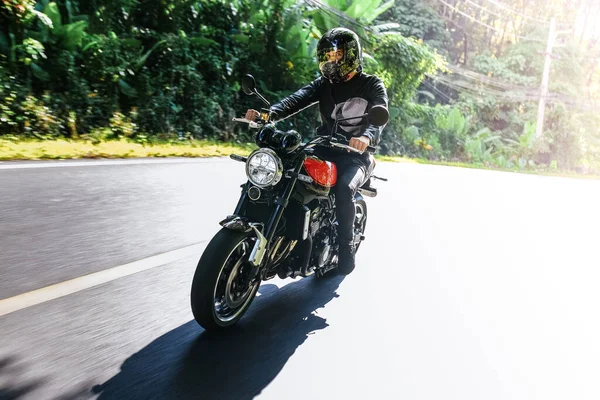 Hombre en un casco monta bicicleta en la carretera entre los trópicos de verano y mira a la cámara —  Fotos de Stock