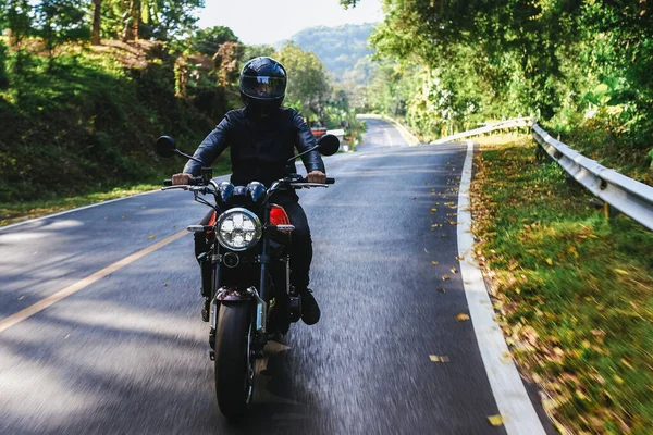 Hombre en un casco negro monta bicicleta en la carretera entre el bosque de otoño —  Fotos de Stock