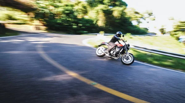 Hombre en casco en motocicleta clásica encaja a su vez en la carretera entre la vegetación —  Fotos de Stock