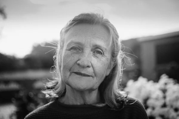 Чорно-білий портрет старшої жінки з сірим волоссям і обличчям зі зморшками на відкритому повітрі, що розслабляються в парку — стокове фото