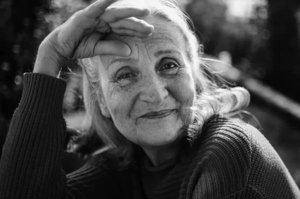 Retrato en blanco y negro de mujer mayor con pelo gris y cara con arrugas al aire libre relajándose en el parque — Foto de Stock