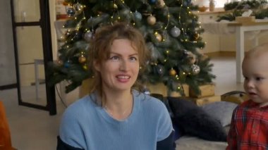 Mutlu aile, evde altın ve gümüş konfetilerle kutluyor. Turuncu koltukta Noel ağacı arka planında oturuyor, gülümseyen bir kadın küçük konfeti parçaları atıyor.