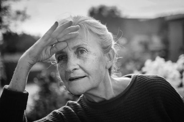 Retrato en blanco y negro de mujer mayor con pelo gris y cara con arrugas al aire libre relajándose en el parque — Foto de Stock