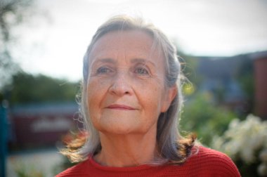 Gri saçlı, kırışık yüzlü, güneşli bir günde parkta dinlenen yaşlı ve güzel bir büyükanne.