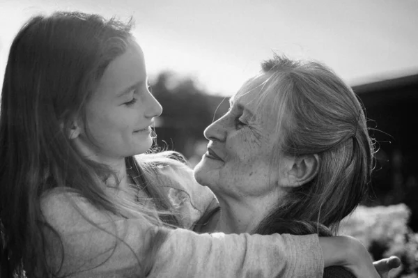 Retrato en blanco y negro de la abuela mayor con el pelo gris con su nieta abrazándose en el jardín y durante el día soleado al aire libre, día de las madres —  Fotos de Stock