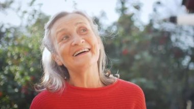 Mutlu gülümseyen, gri saçlı, güneşli bir günde dışarıda kameraya bakan yaşlı kadının yüzünü kapatın.