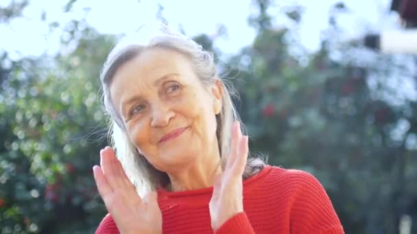 Zamknij twarz szczęśliwej uśmiechniętej starszej kobiety z siwymi włosami patrząc w kamerę podczas spędzania czasu na świeżym powietrzu w słoneczny dzień — Wideo stockowe
