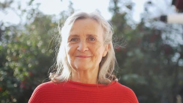 Close up face of senior woman with grey hair looking at camera while spending time outdoors during sunny day — Stock Video