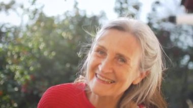 Mutlu gülümseyen, gri saçlı, güneşli bir günde dışarıda kameraya bakan yaşlı kadının yüzünü kapatın.