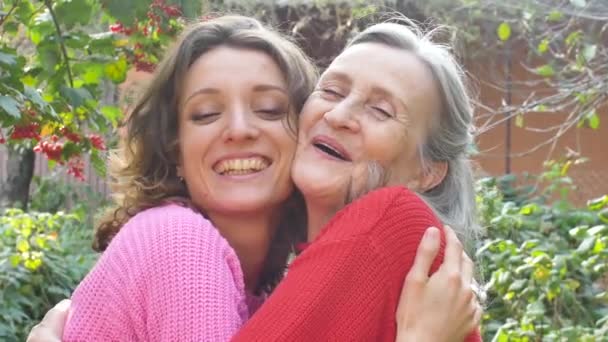 Senior mother with gray hair with her adult daughter looking at the camera in the garden and hugging each other during sunny day outdoors — Stock Video