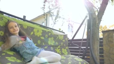 Küçük sarışın kız, yaz boyunca salıncakta sallanıyor güneşli bir günde bahçede oyun oynuyor, mutlu çocukluk konsepti.