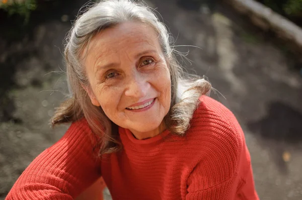 Primer plano retrato de una mujer mayor sonriente con el pelo gris y la cara con arrugas al aire libre relajarse en el parque durante el día soleado —  Fotos de Stock