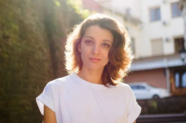 Portrait féminin de belle étudiante, jolie fille aux cheveux courts en t-shirt blanc passant du temps à l'extérieur près d'un vieux mur de pierre lors d'une journée ensoleillée de printemps ou d'été — Photo