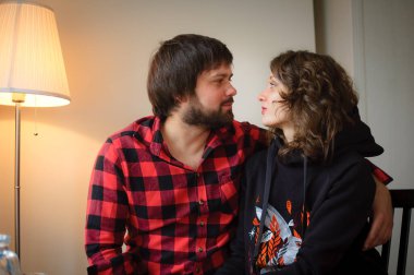 Lambersex tarzı giyinmiş yakışıklı sakallı adam Sevgililer Günü kutlamasında siyah elbiseli genç kadınına sarılıyor.