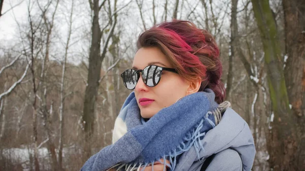 Attraktiv ung kvinna med perfekt hud och makeup med mörkt rosa hår poserar på vintern park bakgrund bär blå halsduk och solglasögon — Stockfoto