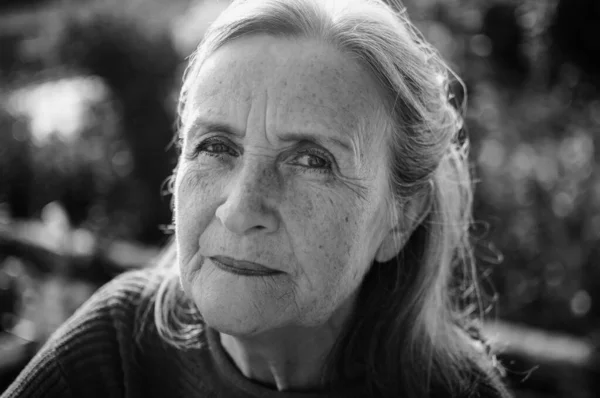 Retrato en blanco y negro de mujer mayor con pelo gris y cara con arrugas al aire libre relajándose en el parque —  Fotos de Stock