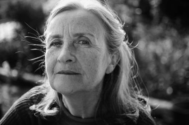 Yaşlı bir kadının siyah beyaz portresi. Gri saçlı ve yüzü kırışıklıklarla dolu. Parkta dinleniyor.