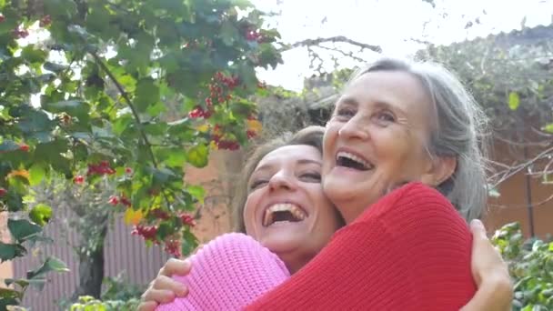 Senior mother with gray hair with her adult daughter looking at the camera in the garden and hugging each other during sunny day outdoors — Stock Video