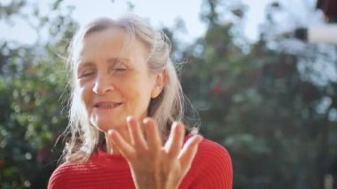 Mutlu gülümseyen, gri saçlı, güneşli bir günde dışarıda kameraya bakan yaşlı kadının yüzünü kapatın.