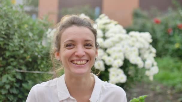 Vrouwelijk model in wit shirt lacht op een achtergrond van park met bloemen tijdens de lente — Stockvideo
