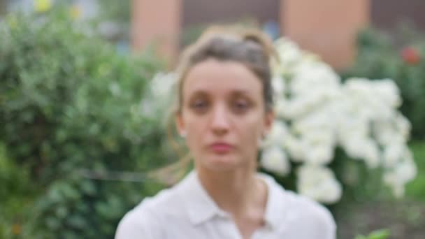 Utomhus kvinnligt porträtt av ung vuxen kvinna i vit skjorta visar sin hand med slogan Jag röstade på blommor bakgrund, val dag koncept — Stockvideo