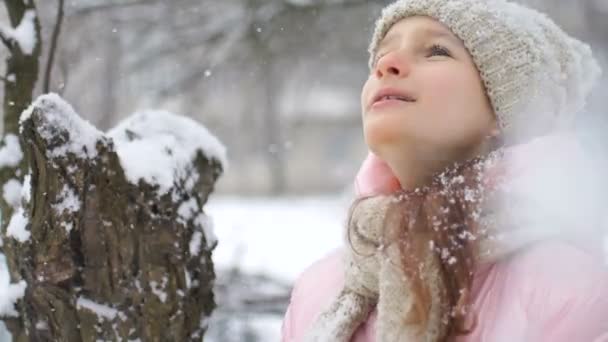 Egy lány, aki télen havazik, nyelves havat eszik, és téli ruhában csukott szemmel néz a szabadba. Boldog gyermekkort és aktív nyaralás koncepció — Stock videók