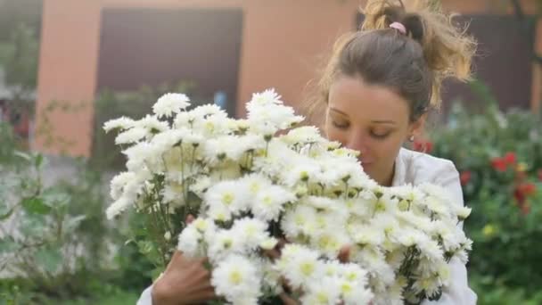 Красивая молодая девушка стоит рядом с кустом белых хризантем в парке в течение весеннего времени, гиперчувствительность, астма, или аллергия концепции — стоковое видео