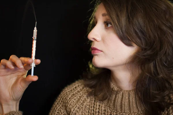Concepto de vacuna. Retrato femenino de una chica caucásica sosteniendo una jeringa y mirándola sobre fondo negro en el estudio. —  Fotos de Stock