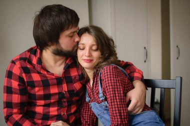 Benzer kırmızı kareli gömlekler giyen sevimli çift, Sevgililer Günü kutlamaları sırasında evde oturmuş birbirlerine sarılıyorlar. Erkek ve kız arkadaşının kapalı bir portresi.