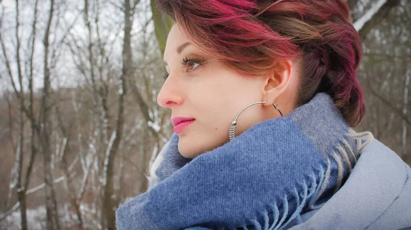 Attraktiv ung kvinna med perfekt hud och makeup med mörkt rosa hår poserar på vintern park bakgrund bär blå halsduk och silver örhängen — Stockfoto