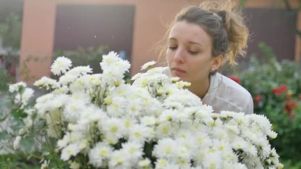 Gadis cantik muda berdiri di dekat semak-semak chrysanthemums putih di taman selama musim semi, hipersensitivitas, asma, atau alergi konsep — Stok Video